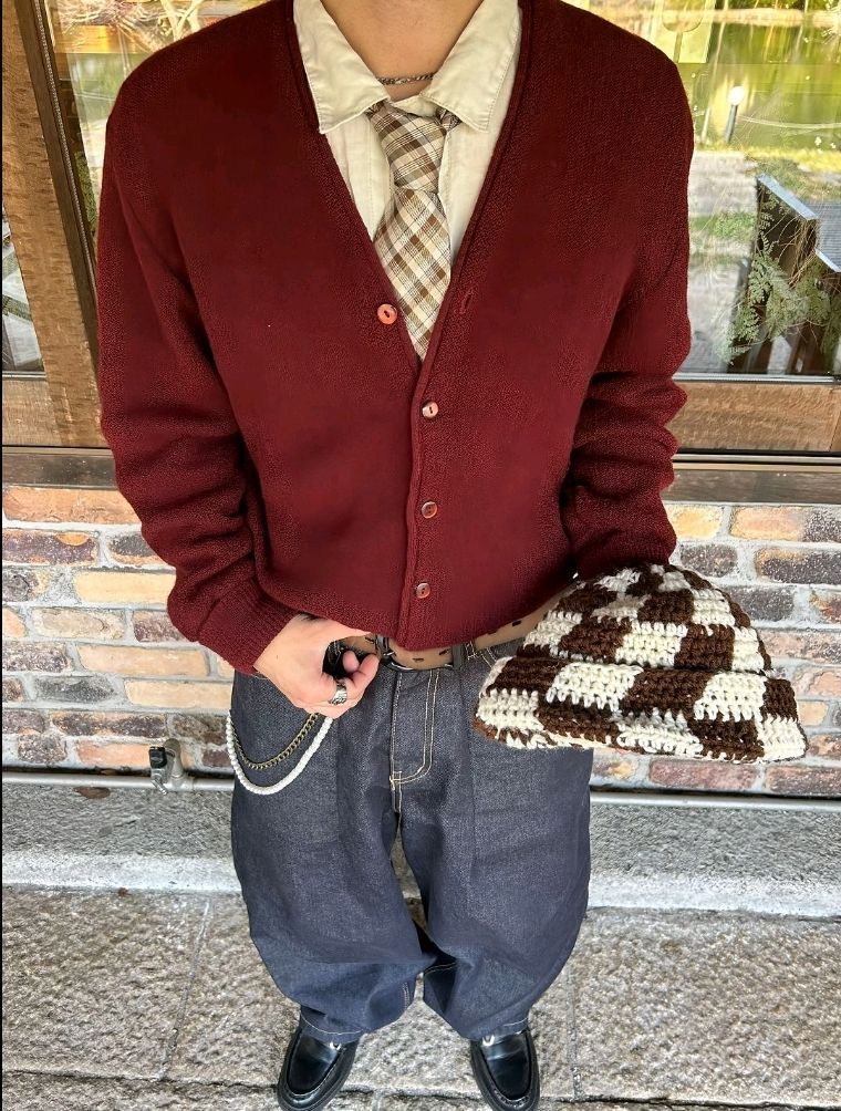 Un homme avec cardigan rouge avec un bonnet dans la main dans la rue 